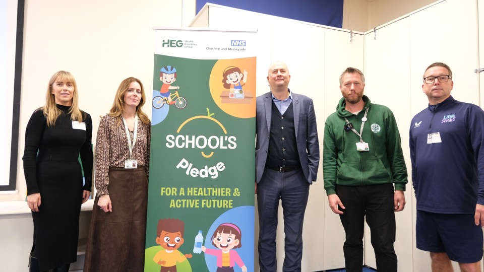 Five people stand beside a colourful banner reading "School's Pledge: For a Healthier & Active Future."