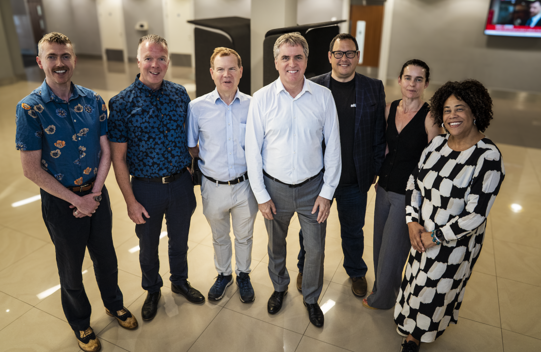 A group of seven people posing together in a modern building hallway.