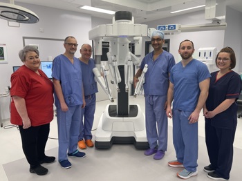 A large white robot with six people stood around it, they are in a hospital with scrubs on.