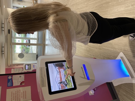 A woman with her left arm outstretched, using a touch screen sign-in kiosk