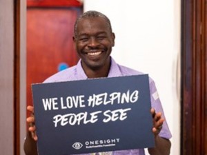 A man holding a sign which says "we love helping people see"