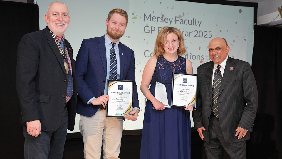 Four people stand smiling on a stage. Two in the centre hold framed awards. A screen behind them reads, "Mersey Faculty GP Registrar Award 2025."